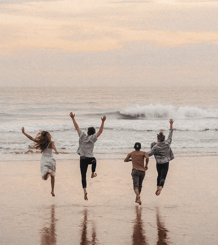 Four friends running together toward the ocean at sunset.