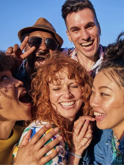 A close group selfie of friends smiling together in bright sunlight.