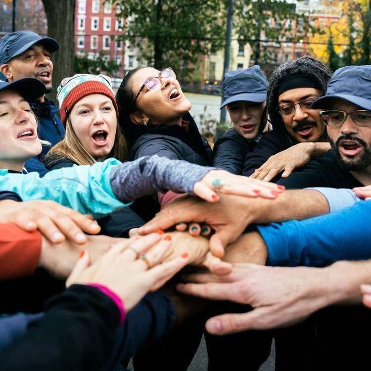 A group of people reaching in together with their hands stacked in a shared huddle.